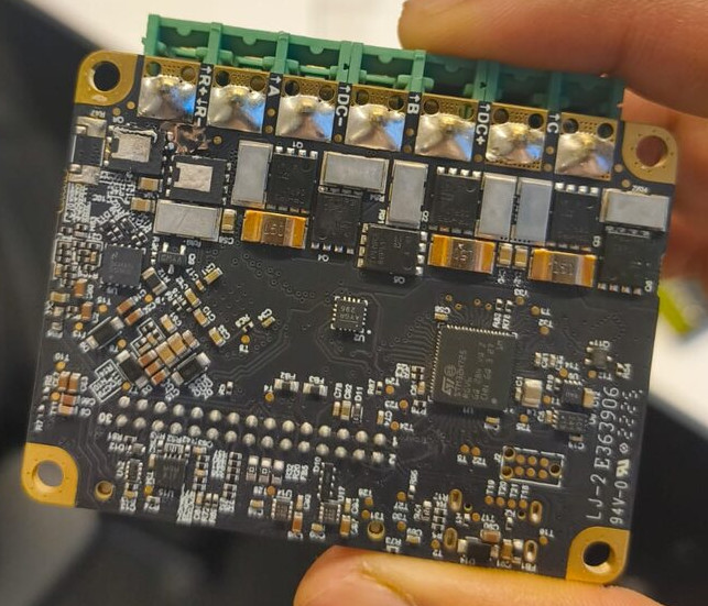 A motor controller board being inspected by hand, with a scorched, discolored patch near one of the terminal connectors.