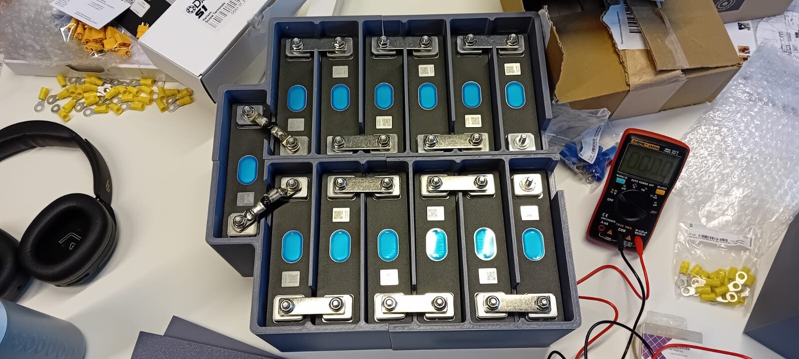 Lithium battery pack under assembly with terminal hardware and a multimeter for cell verification.
