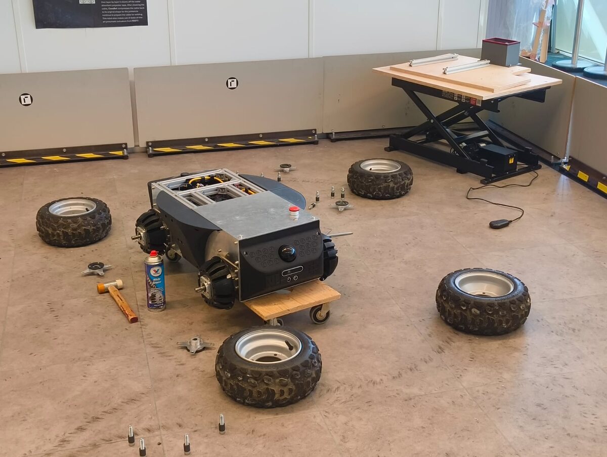 SLIP's chassis stripped down for wheel and hub repair, wheels removed and laid out around it with tools, white grease, and a mallet.